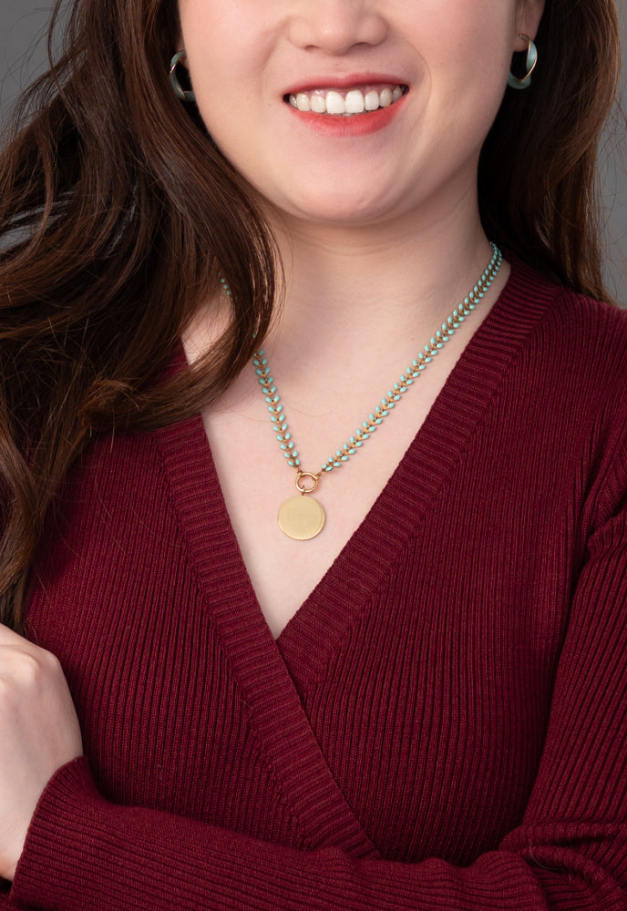 Smiling model in a burgundy sweater wearing engravable round pendant on mint Seeds of Hope chain