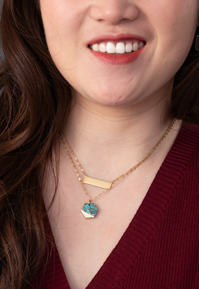 Close-up of model wearing engravable gold bar necklace layered with a turquoise pendant