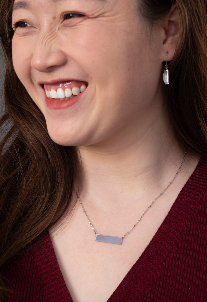 Smiling model in a burgundy top wearing the engravable silver bar necklace