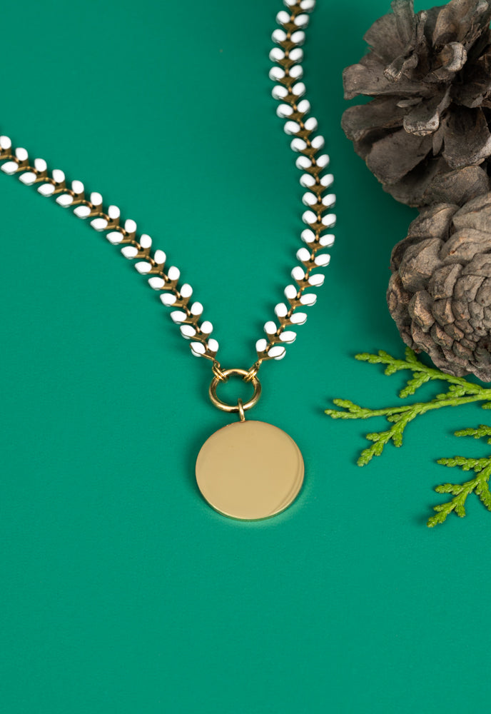 Engravable round gold pendant on ivory Seeds of Hope chain on green with pinecones