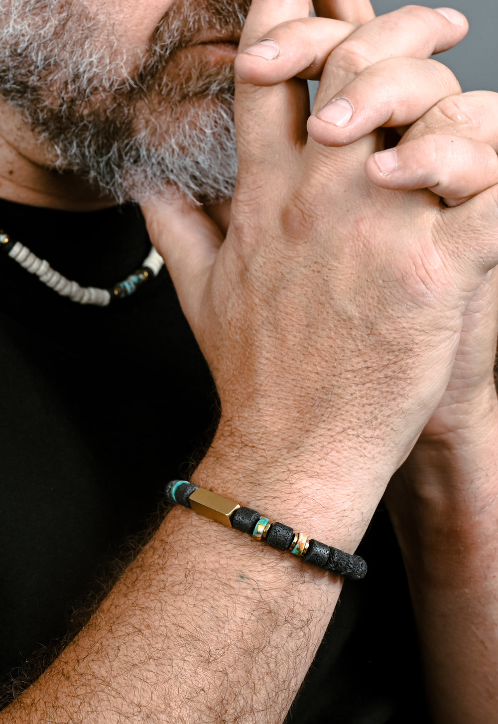 Close-up of man with clasped hands wearing a beaded necklace and bracelet