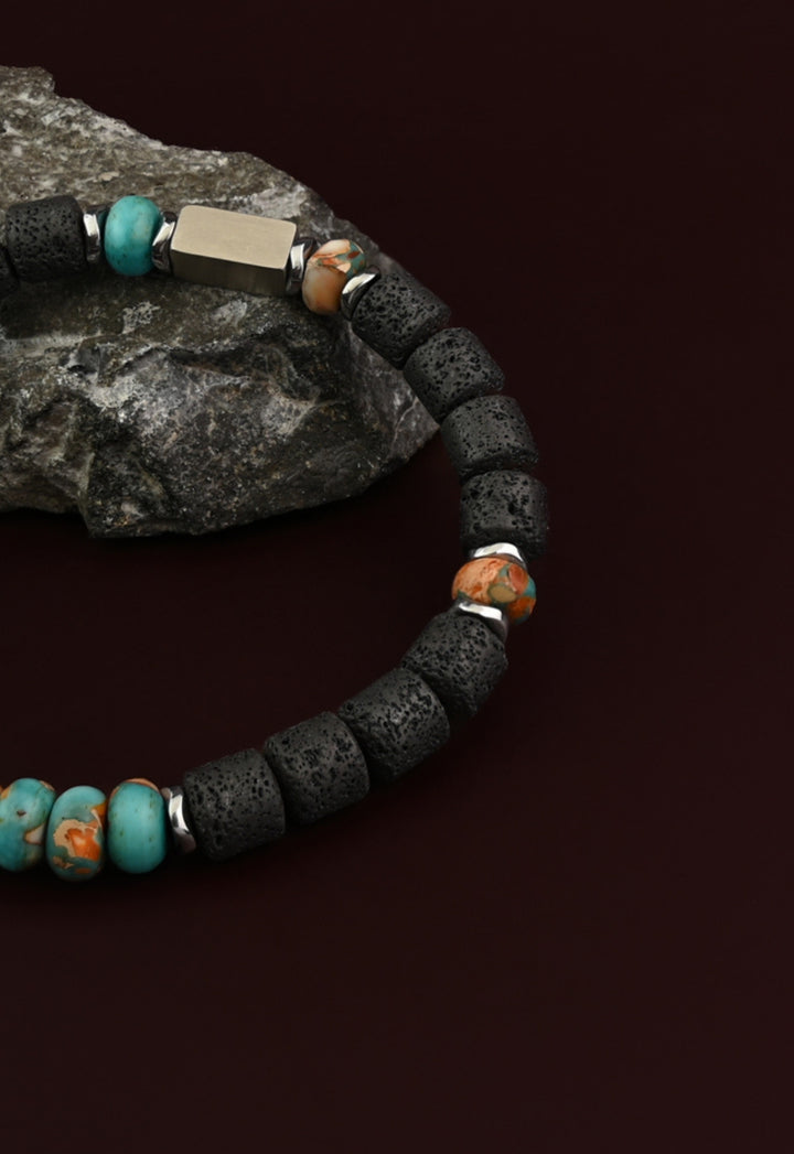 Strength lava bead and turquoise emperor stone bracelet on a gray rock