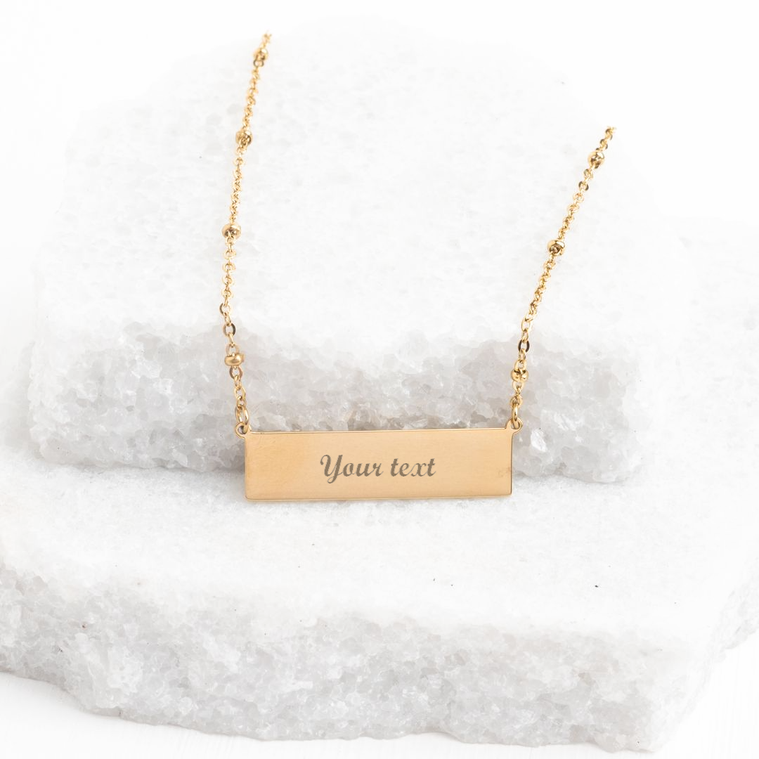 Engravable gold bar necklace with sample "Your text" engraving on white stone