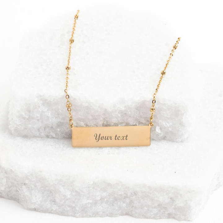 Engravable gold bar necklace with sample "Your text" engraving on white stone