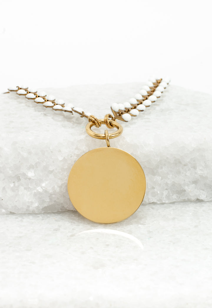 Close-up of blank gold round pendant on ivory Seeds of Hope chain on white stone